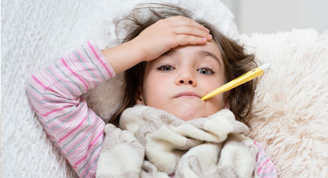 A young girl who looks ill holding her hand to her forehead with a thermometer in her mouth